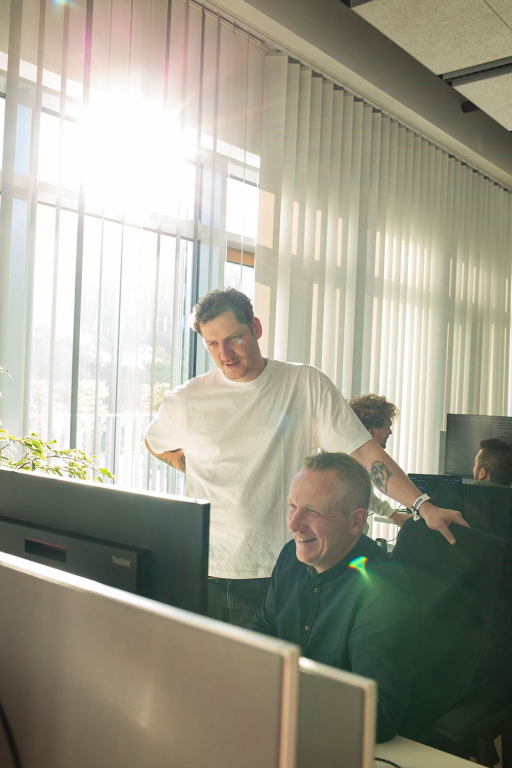 Teamarbeit im Büro: Domi und Olli lachen gemeinsam vor einem Computerbildschirm.